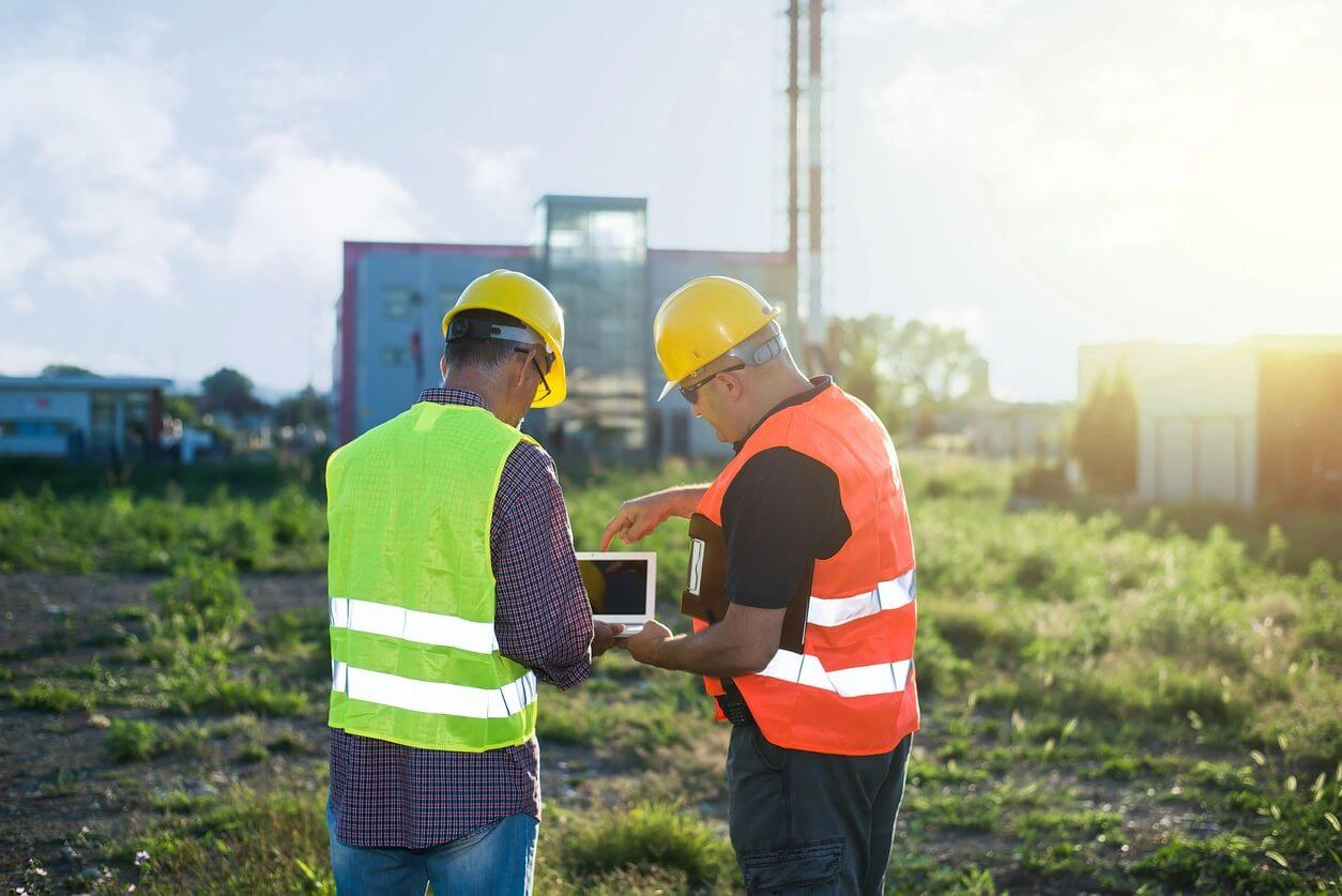 Two men in safety vests and hard hats looking at a tablet.